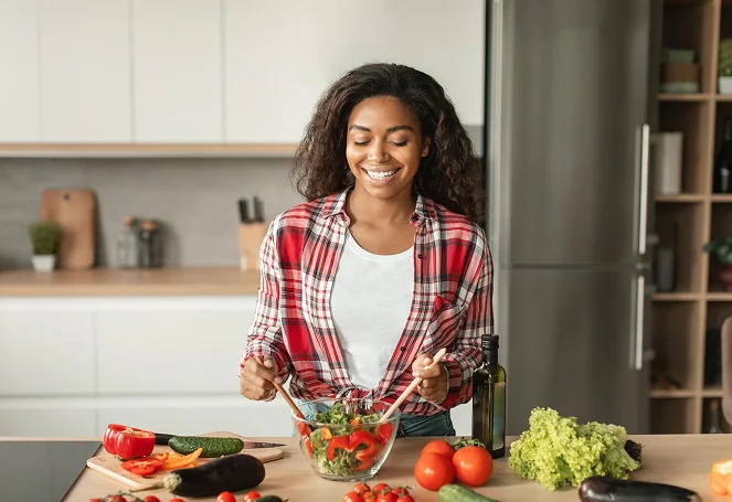 A smiling woman tossing a fresh vegetable salad in a modern kitchen