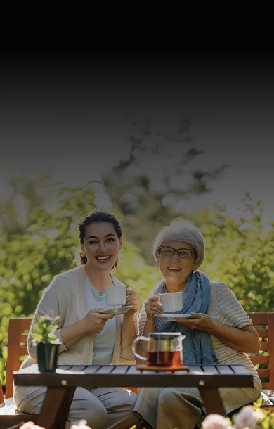 A caregiver and senior woman smiling while sharing tea together in a sunny garden
