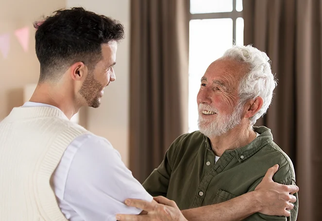A young man and smiling elderly man embracing warmly indoors