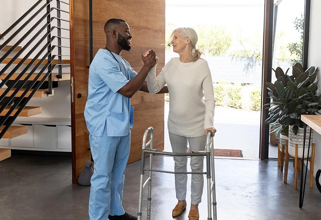A caregiver helping an elderly woman with a walker near a home entrance