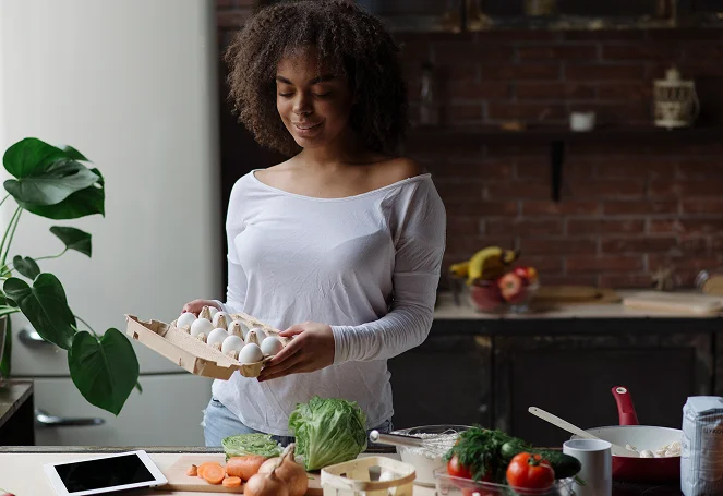 A woman preparing a meal in a kitchen holding a carton of eggs