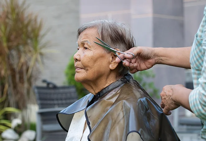 An elderly woman getting her hair trimmed with scissors outdoors