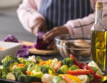 Person preparing a colorful assortment of fresh vegetables including broccoli, bell peppers, and cauliflower on a kitchen counter with a bottle of olive oil nearby