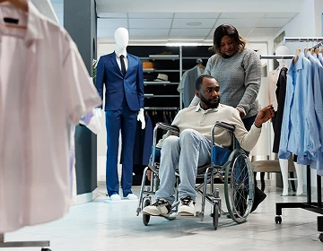Caregiver assisting a man in a wheelchair while shopping for clothes in a clothing store