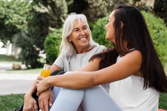 Smiling elderly woman and a younger woman talking together while sitting outdoors in a park after exercise