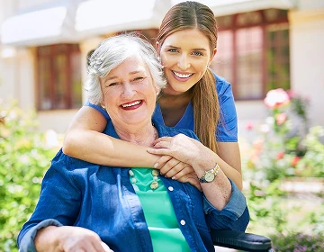 Smiling caregiver embracing a happy elderly woman in a wheelchair in a sunny garden